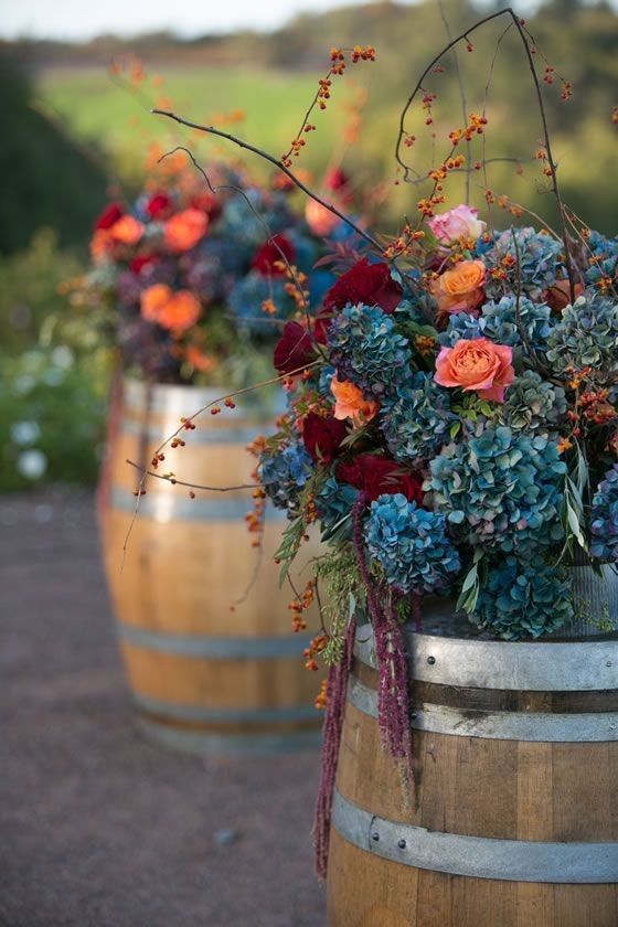 Blue hydrangea and branches atop wine barrels are...